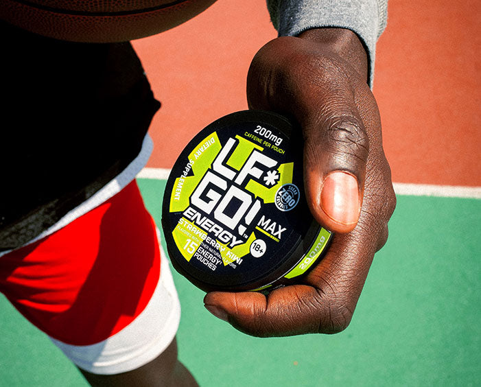 Man in red shorts holding a can of LFGO Strawberry Kiwi energy pouches towards the camera while standing on a basketball court