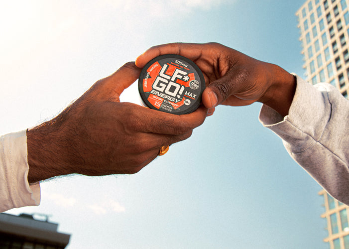 Two hands coming together as they both hold a single can of LFGO Sour Cherry energy pouches against the backdrop of a blue sky. 